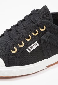 Schwarze Canvas-Sneaker mit goldenen Ösen, weißer Gummisohle und strukturiertem Finish sowie einem "Superga"-Label an der Seite.