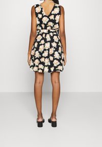 Černé šaty s květinovým potiskem a V-výstřihem, přiléhavého střihu, s lehce oranžovými růžemi a páskem v pase; nošeny s černými blokovými podpatky.