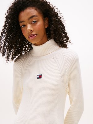 Maglione a collo alto a coste color crema con un design aderente e una piccola etichetta con il logo Tommy Jeans sul lato sinistro del petto.