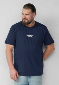 Granatowa koszulka bawełniana z krótkim rękawem, z białym nadrukiem logo po lewej stronie klatki piersiowej. Prosty design, okrągły dekolt.