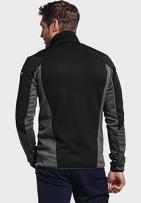 Schwarze und graue Fleecejacke mit hohem Kragen, die kontrastierende Seitenpaneele und lange Ärmel aufweist. Glatte Textur und taillierter Schnitt.