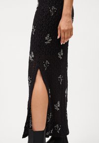 Fustă tricotată neagră cu broderie florală, având o fanta laterală și un material texturat. Accentuată cu fire metalice pentru detalii.