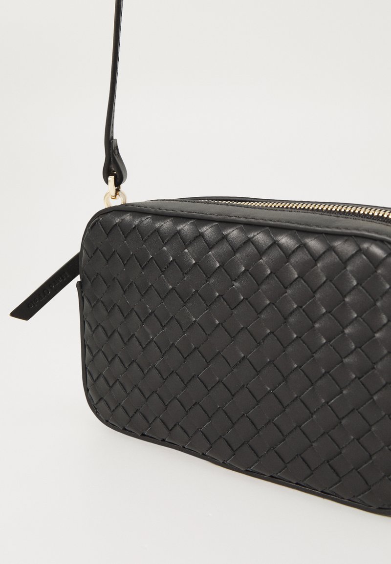 Schwarze Leder-Clutch mit geflochtenem Muster, goldfarbener Reißverschlusstechnik und abnehmbarem Tragegurt. Rechteckige Form, kompaktes Design.