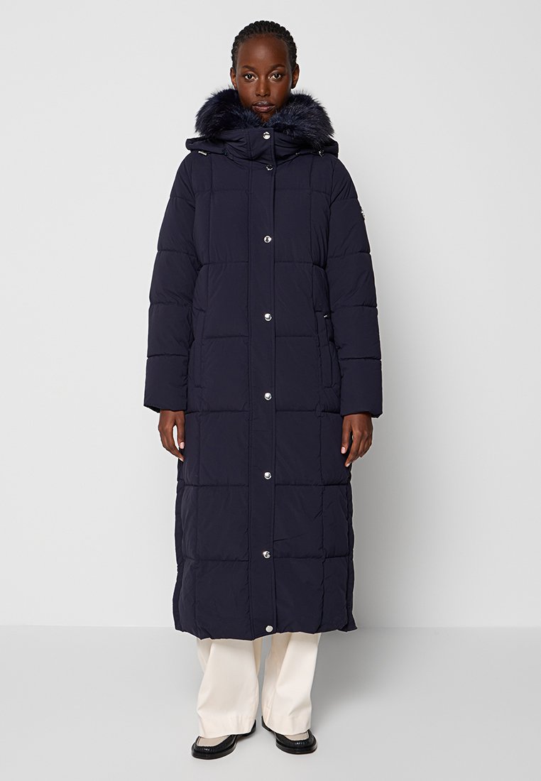 Cappotto puffer lungo color navy con cappuccio foderato in pelliccia, bottoni a pressione, tasche laterali e design trapuntato. Il tessuto appare liscio con una leggera lucentezza.