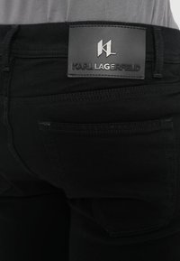 Μαύρο τζιν από denim με υφασμένο δερμάτινο μπαλώμα που φέρει το λογότυπο "Karl Lagerfeld" και τα αρχικά "KL". Ορατές πίσω τσέπες και ραφές.