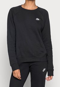 Felpa nera realizzata in tessuto morbido, con colletto rotondo e polsini a coste. Piccolo logo bianco Nike sul petto, abbinata a pantaloni coordinati.