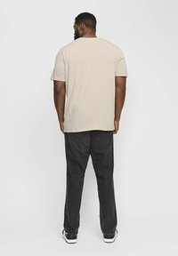 T-shirt beige à manches courtes avec un col rond, associé à un pantalon en denim gris foncé et des baskets noires. Design simple sans motifs.