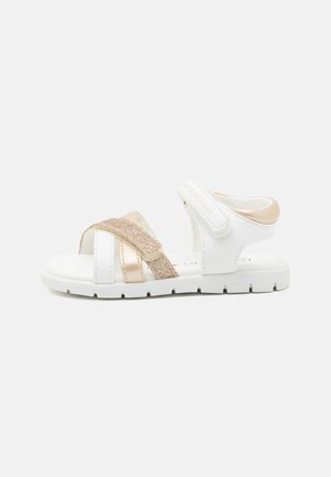 White sandals with metallic rose gold accents, featuring adjustable straps and a textured finish, designed for comfort and support.
