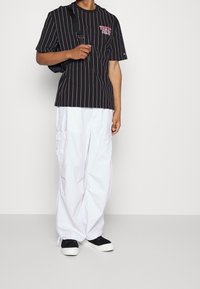 Black and white striped t-shirt with round neck, paired with loose white cargo pants and black sneakers. Simple design with casual fit.