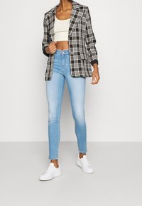 Blazer a cuadros en blanco y negro con un solo botón, combinado con jeans ajustados de color azul claro y zapatillas blancas. Tejido suave, corte relajado.