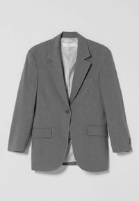 Ein grauer Blazer mit einem Knopf, spitzen Revers, zwei vorderen Klappentaschen und einer Brust-Paspeltasche, flach auf einem weißen Hintergrund präsentiert.