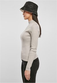 Vaaleanharmaa ribbipinta turtleneck-neule, joka on yhdistetty tummiin farkkuihin. Mallilla on päässään musta saarikypärä, jossa on vaaleanbeige vuori.
