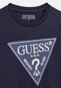 Maglietta blu navy realizzata in cotone biologico, con una grande toppa triangolare blu con scritte bianche e una texture trapuntata.