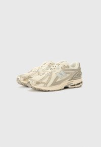 Beige running shoes with mesh upper, reflective accents, and cushioned sole. Features laces and curved design for comfort and support.