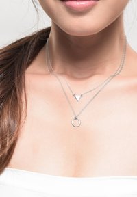 Sølvlagde halskæder med et trekant- og et cirkelvedhæng, med fine kæder og en poleret finish, hviler på bar hud.