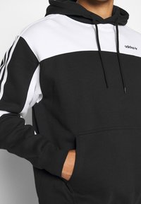 Svart och vit huvtröja med en framficka, kontrasterande färgbockning och dragsnören, tillverkad av mjuk bomullsblandning.