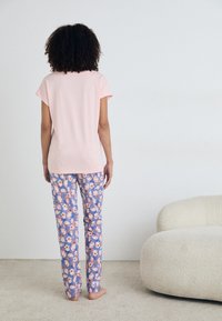 Šviesiai rožinė medvilninė marškinė su trumpomis rankovėmis, derinama su mėlynomis kelnių su gėlių raštais. Minkštas audinys, laisvas siluetas.