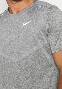 Camiseta deportiva de manga corta en gris con una textura jaspeada. Cuenta con un escote redondo y un logo de Nike en blanco en el pecho.