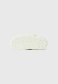 Vit sula av en fluffig ljusgrön Crocs-sandal med mönster på sulan, uppställd mot en enkel vit bakgrund.