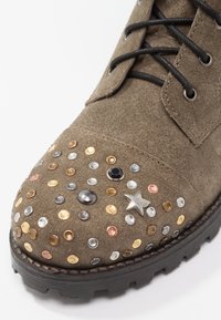 Hnědé semišové boty s kovovými hroty v různých barvách, s hvězdným akcentem a černými tkaničkami. Texturovaný povrch a robustní černá podrážka.