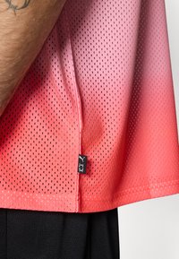 T-shirt de sport perforé en dégradé de nuances corail, avec une étiquette à l'ourlet. Le matériau est respirant et texturé pour une performance optimale.