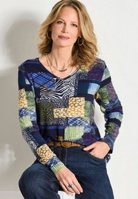 Langärmliges Oberteil mit einem Patchwork-Design, das verschiedene Muster in Blau, Grün, Gelb und Schwarz auf einem dunklen Hintergrund zeigt.
