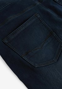 La tela de denim azul oscuro cuenta con un solo bolsillo trasero con un diseño de costura triangular y un doble detalle de costura en contraste.