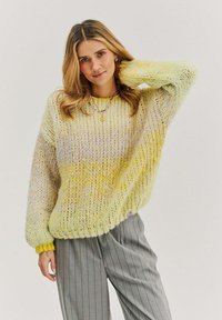 Prehnutý pletený sveter v gradientných žltých odtieňoch s texturovanou priadzou. Rybárske manžety a lem, v kombinácii so šedými pruhovanými nohavicami.