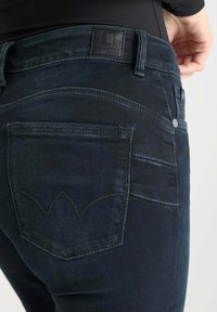 Donkerblauwe denim jeans met een slimfit ontwerp. Heeft een gestructureerde achterzak met een onderscheidend gestikt patroon. Inclusief een leren label aan de taille.