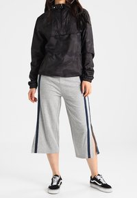 Svart kamouflagepulloverjacka med halv dragkedja och elastiska ärmar, tillsammans med grå culotter med marinblå sidostrecken och sidofickor, bärs med svarta sneakers.