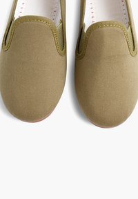 Scarpe slip-on in tela verde oliva con una finitura testurizzata, dettagli elasticizzati all'apertura e una suola in gomma rossa a contrasto.