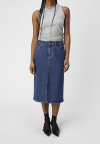 Gonna midi in denim blu scuro, con una fessura anteriore, cinque tasche e passanti per cintura. Abbinate a un top senza maniche grigio chiaro e tacchi neri.