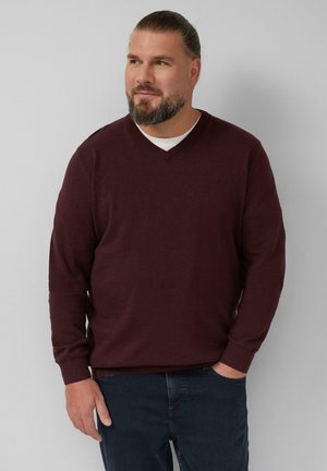 Bordeaux V-hals trui gemaakt van zachte gebreide stof, met lange mouwen en een geribbelde zoom. Draagt over een wit shirt met donkere jeans.
