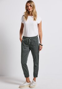 Vit kortärmad topp med rundad halsringning i kombination med mörkgröna smalnande joggingbyxor med elastisk midja och sidofickor.