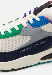 Zapatilla verde, azul, gris y marino con materiales de malla y ante; presenta cordones blancos, acentos texturizados y la marca "ARMANI EXCHANGE".