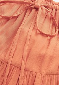 Tissu corail clair avec un cordon noué à la taille et un matériau froncé et texturé sous la couture.