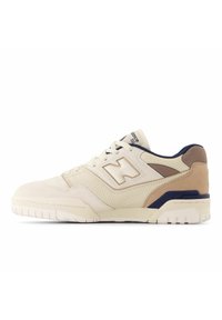Beige athletic shoe with suede and mesh materials, featuring a perforated design, padded collar, and navy and tan accents. Thick white sole.