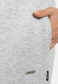 Lichtgrijze katoenen sweatpants met een gestructureerde stof, zijzak en een aangebracht label met de tekst "SMILOOXX" nabij de zoom.