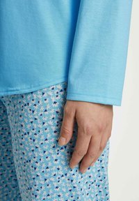 Lichtblauw langemouwen shirt met een gladde textuur, gecombineerd met gestreepte blauwe pyjamabroek met kleine bloemen- en bladmotieven in wit en donkerblauw.