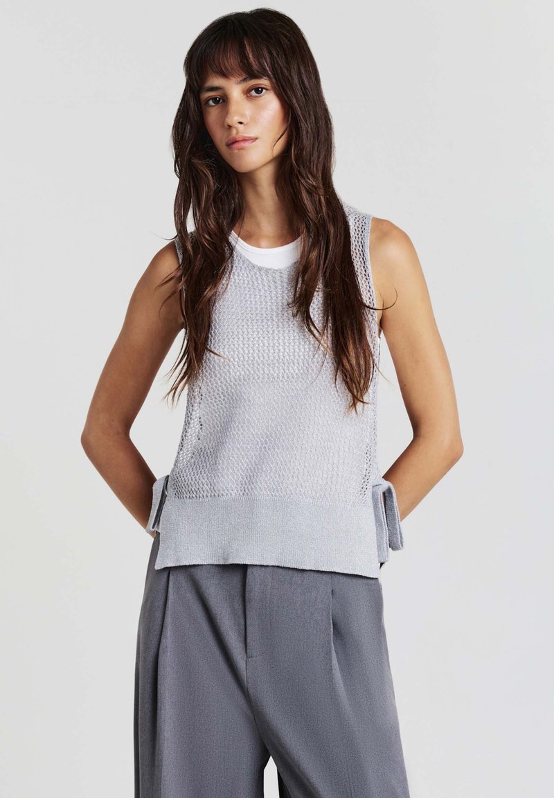 Top senza maniche grigio a maglia con un design testurizzato, scollo a girocollo e legature laterali, abbinato a pantaloni grigi larghi.