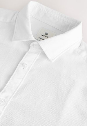 Hvid tekstureret poloshirt med en bred krave og tre knapper, med et "NEXT" mærke inde i kraven.