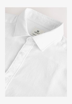 Fehér, texturált pólóing széles gallérral és három gombbal, a gallér belsejében "NEXT" márkajelzéssel.