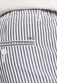 Stribede bukser i sort og hvid bomuld med en tekstureret overflade, der har en forlommer og et metal logo-tag på siden.