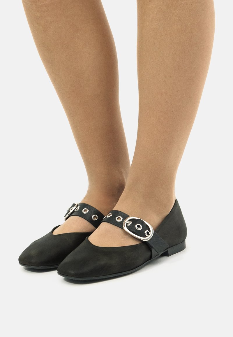 Bailarinas de ante negro con punta afilada y una correa ancha con herrajes de plata. La suela es plana y ofrece un diseño minimalista.