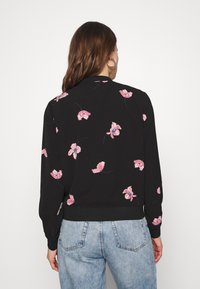 Svart tröja med blommönster som har rosa blommor, ribbat avslut vid ärmar och fåll, samt långa ärmar. Bärs tillsammans med ljusblå högmidjade jeans.