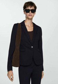 Blazer nero su misura con un solo bottone, abbinato a una borsa a spalla in suede marrone e occhiali da sole scuri. Texture liscia, forma strutturata.
