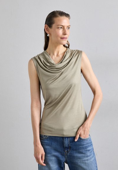 Ärmelloses Top mit drapiertem Kragen aus weichem, olivgrünem Stoff, kombiniert mit blauen Jeans. Glatte Textur, figurbetonter Schnitt.