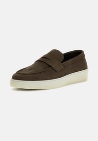 Zapato marrón de ante sin cordones con una banda acolchada en la parte superior, que presenta una suela de goma blanca y detalles de costura en los bordes.