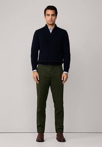 Marinblå stickad tröja med halvpolo och dragkedja, kombinerad med olivgröna byxor och bruna ankelboots. Mjuka material och figurnära design.