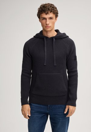 Donker gebreide hoodie met een textuurpatroon, trekkoord kap, voorzak en geribbelde manchetten en zoom, gecombineerd met blauwe jeans.